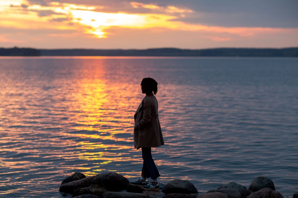 Person sitting peacefully beside a lake at sunrise, reflecting calmly after letting go of emotional resistance