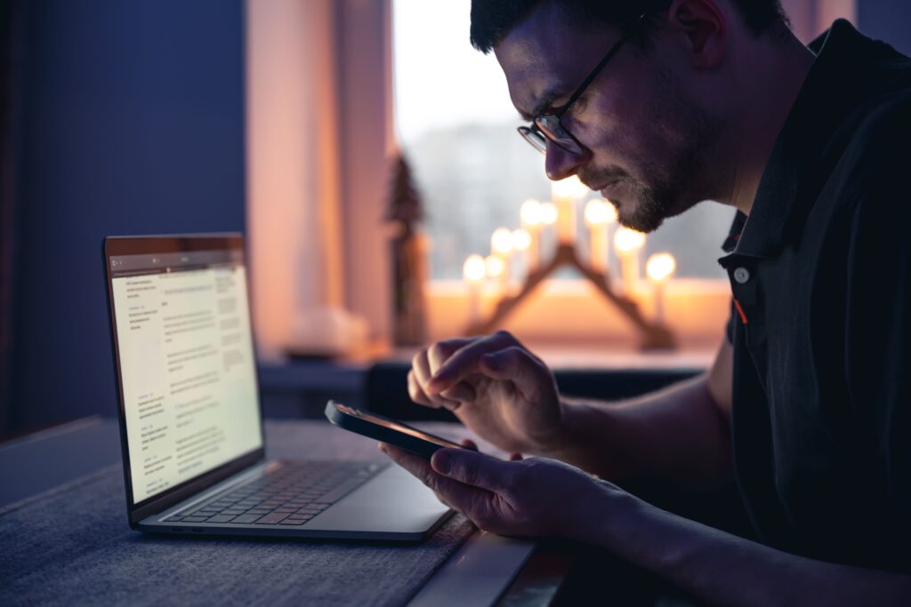 Split illustration showing part of a person's attention remaining on a smartphone while trying to work on a laptop