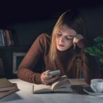 Person looking overwhelmed while sitting at a desk surrounded by smartphone notifications and digital distractions