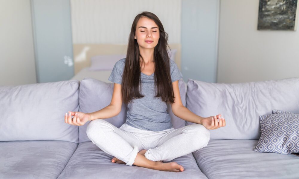 Person relaxing on a comfortable sofa after a stressful day while practicing deep breathing in a peaceful living room