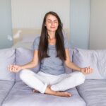 Person relaxing on a comfortable sofa after a stressful day while practicing deep breathing in a peaceful living room