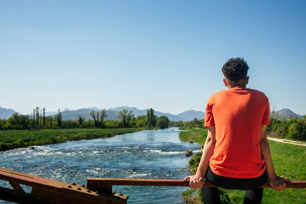 Person standing peacefully beside a flowing river, symbolizing acceptance of situations beyond personal control
