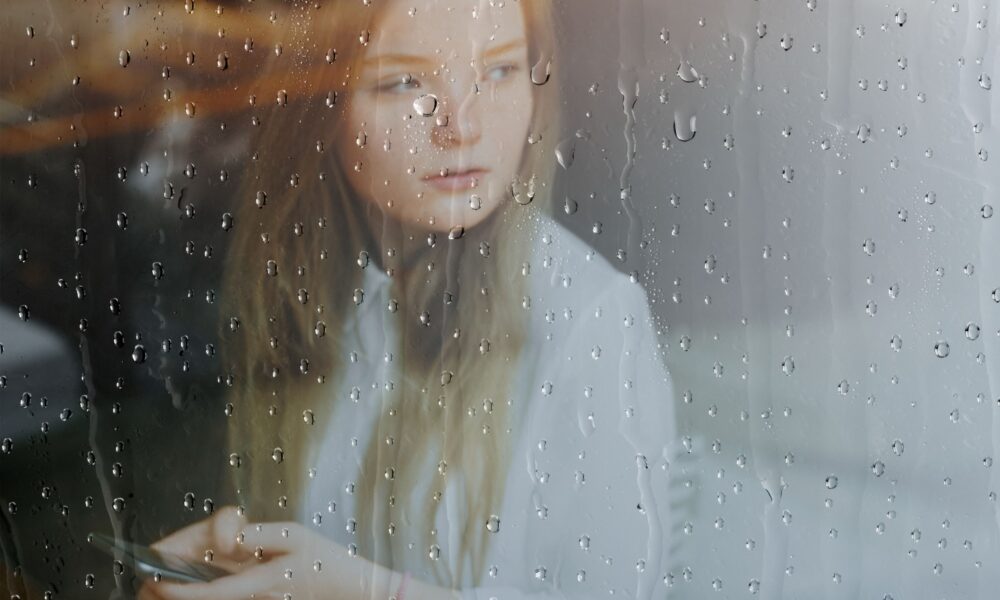 Person sitting quietly by a rain-covered window, reflecting calmly during a period of uncertainty and emotional stress