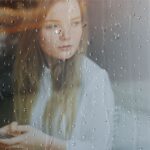 Person sitting quietly by a rain-covered window, reflecting calmly during a period of uncertainty and emotional stress