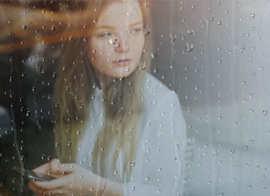 Person sitting quietly by a rain-covered window, reflecting calmly during a period of uncertainty and emotional stress
