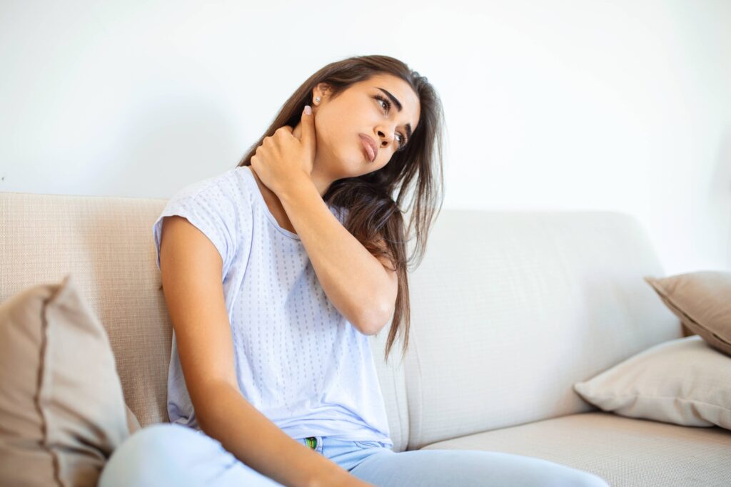 Person sitting on a sofa rubbing their neck and shoulders after a demanding day