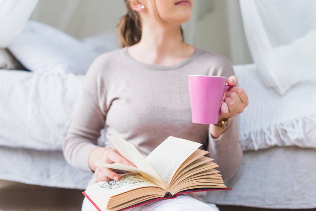 Person reading a book with a cup of herbal tea instead of using a smartphone before bed