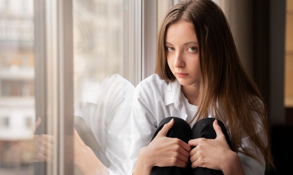 Young professional sitting quietly by a window feeling anxious despite nothing obviously being wrong