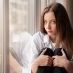Young professional sitting quietly by a window feeling anxious despite nothing obviously being wrong