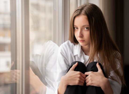 Young professional sitting quietly by a window feeling anxious despite nothing obviously being wrong